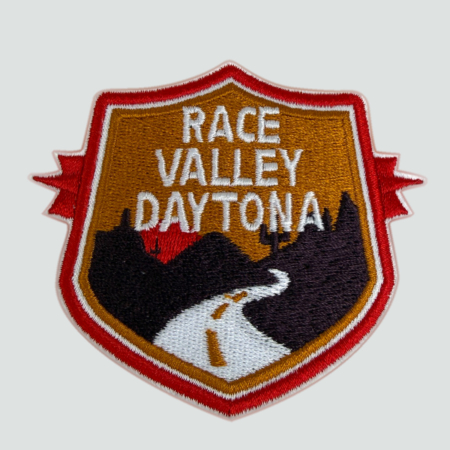 Embroidered Racing Relics “Race Valley Daytona” patch featuring a desert road and mountain backdrop in red, gold, and black.